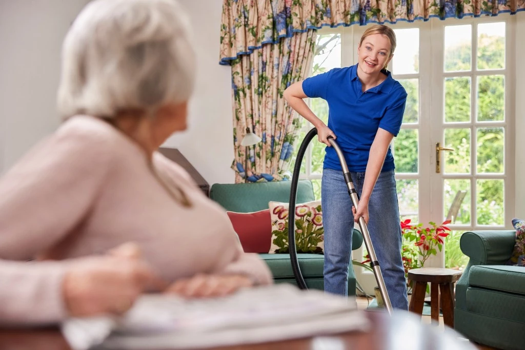 Carer vacuuming home of elderly woman