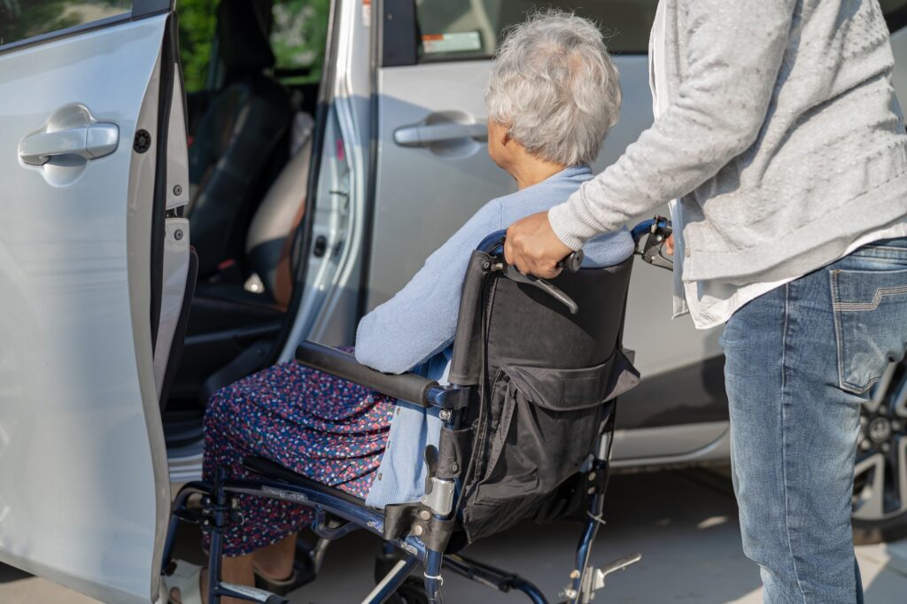 Help and support asian senior woman patient sitting on wheelchair prepare get to her car